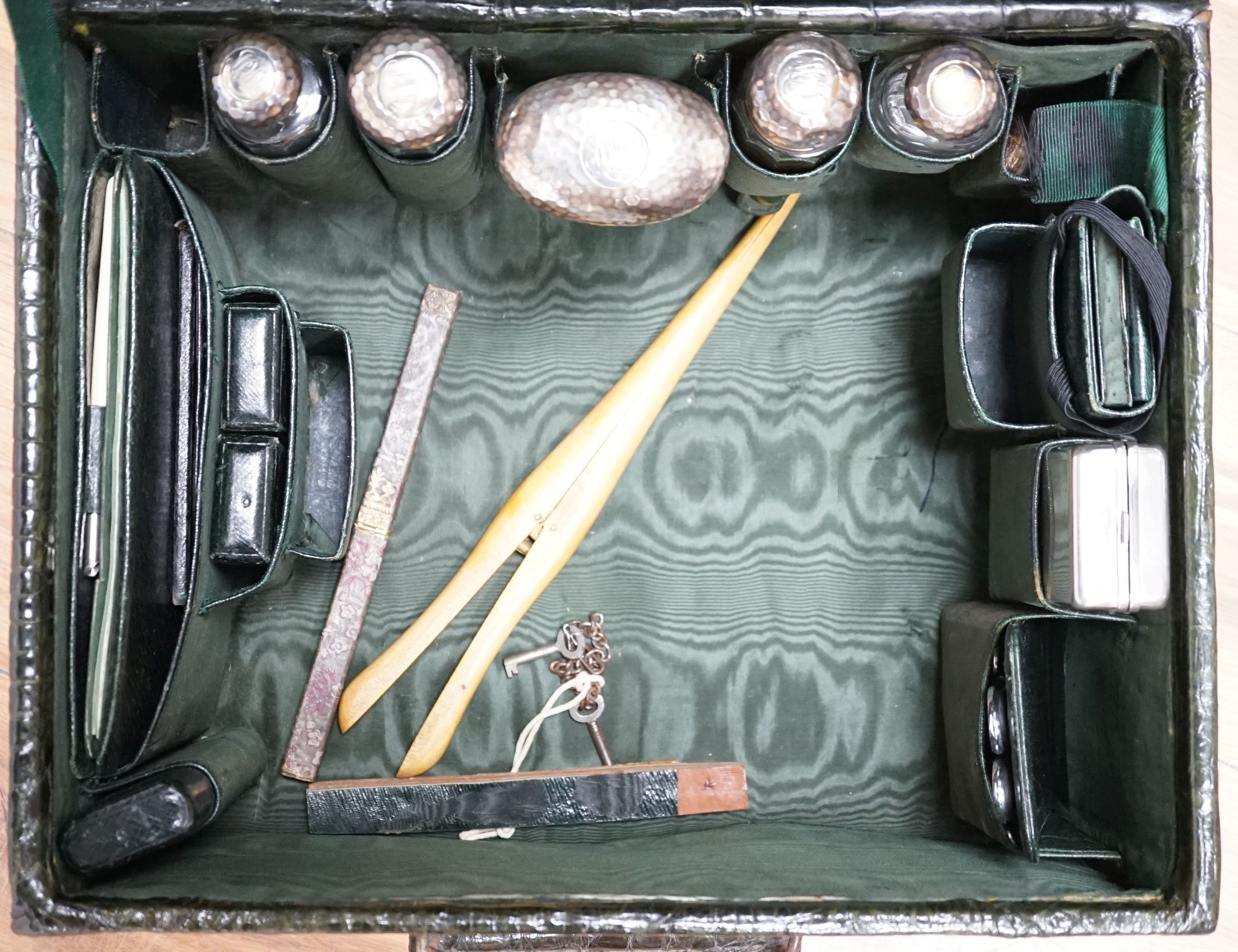 An early 20th century green crocodile toilet case with silver mounted interior, width 39 cms.